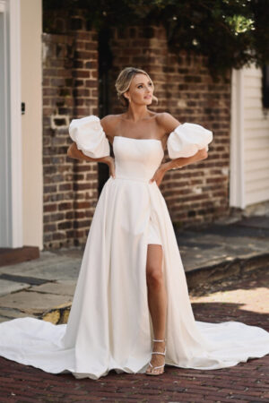 Understated elegance with a contemporary twist, Style D3957 transforms into two stunning bridal looks for that special day. The short strapless mini wedding dress features a softly scooped neckline to introduce the clean, modern aesthetic of this modern bridal look. To elevate the look, detachable puff sleeves sit just off the shoulder and a detachable satin overskirt adds a touch of drama and a sexy high leg slit that reveals the short wedding dress beneath. The modern simplicity of this chic wedding gown offers versatile options to tailor to a contemporary wedding day look that is unique to every bride.